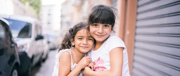 Two young sisters embracing and smiling on a city street