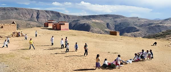 Rural schoolyard with children in white tops, mountainous landscape with brick