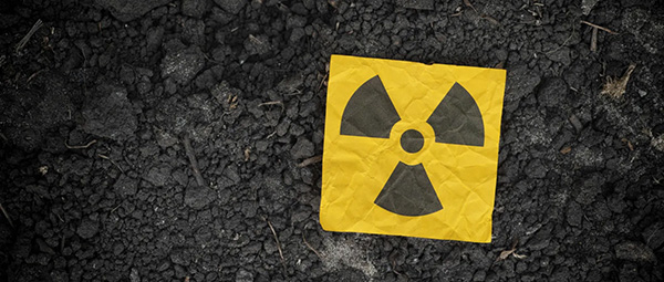 Crumpled yellow paper with a black radiation symbol resting on dark, rocky ground.