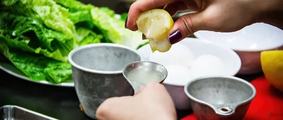 A person preparing food by adding fresh lemon juice, demonstrating hands-on work in a nutrition or foodservice systems environment.