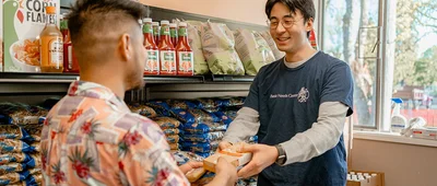 A student volunteer at a university Basic Needs Center assists a peer with food selection, highlighting campus resources for community nutrition and student support.