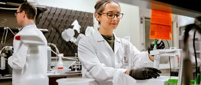 Two researchers in white lab coats working in a scientific laboratory setting with various equipment and containers.