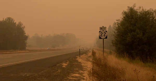 A highway is shrouded in thick orange haze from wildfire smoke