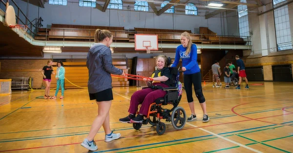 A group of people, including a person in a wheelchair, participating in an activity in a gymnasium.
