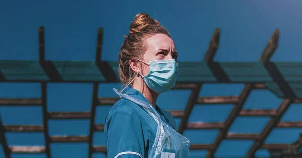 A woman wearing a medical face mask standing in front of a blue background.