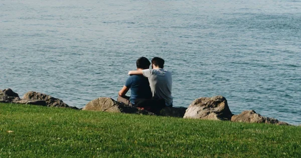 Two people sitting on a grassy hill overlooking the ocean.