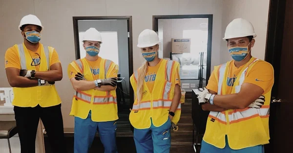 Four althetic training interns wearing San Diego Chargers themed hard hats and safety vests standing together.