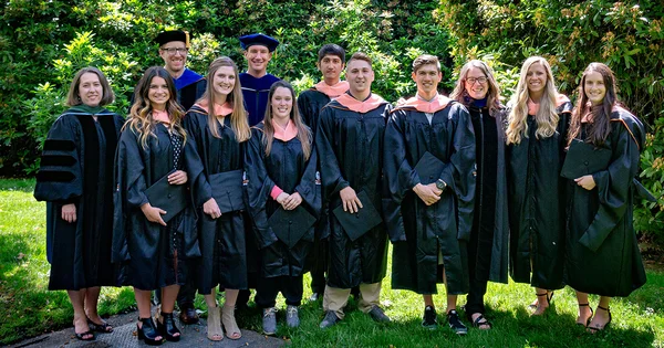A group of graduates in academic regalia posing for a photo outdoors.