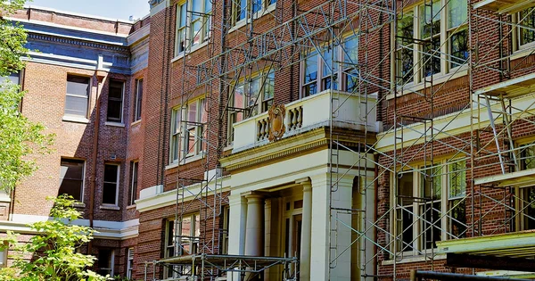 Historic brick building with scaffolding during renovation, featuring classical architectural elements and multiple windows.