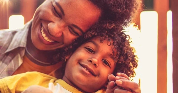 A warm, intimate portrait of a caregiver and child with curly hair, sharing a tender moment with soft, golden lighting.