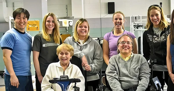 Group photo of six people in an office or workplace setting, with two individuals in wheelchairs.