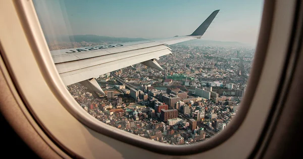 View of a dense urban landscape through an airplane window with a wing visible.