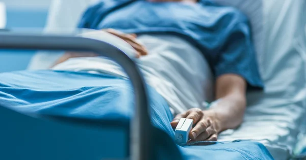 person laying in hospital bed with a finger pulse oximeter