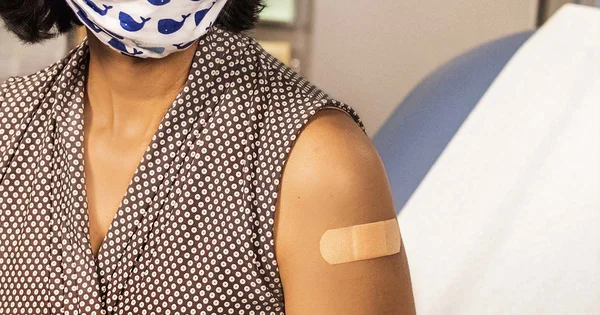 Person wearing a whale-patterned face mask and polka dot top with a bandage on their upper arm.
