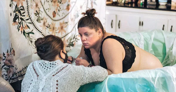 Waterbirth with expectant mother in inflatable pool and a doula offering support.