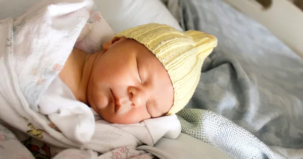 Sleeping newborn wearing a yellow knitted hat, wrapped in soft blankets.