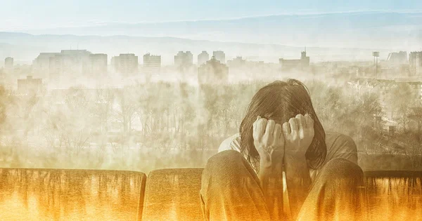 A person sitting with their head in their hands, overlaid with a cityscape in sepia tones, suggesting emotional distress or isolation.