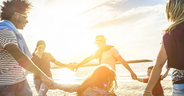 Group of people holding hands in a circle on a beach at sunset, with warm golden light and ocean in background.