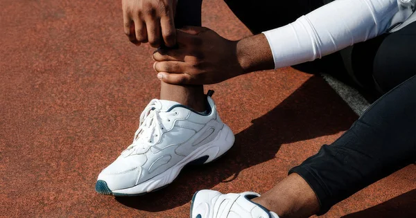 An athlete's hands grasp their ankle, indicating a moment of discomfort, stretching, or injury during physical activity, relevant to sports medicine or rehabilitation contexts.
