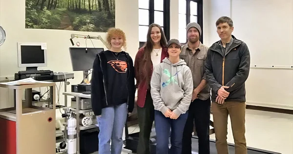 Five team members standing together in a lab setting, with equipment and a scenic picture in the background.
