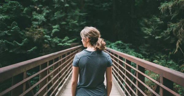 A woman on a bridge leading into a dark forest, symbolizing a journey, making a choice, or facing a path ahead.