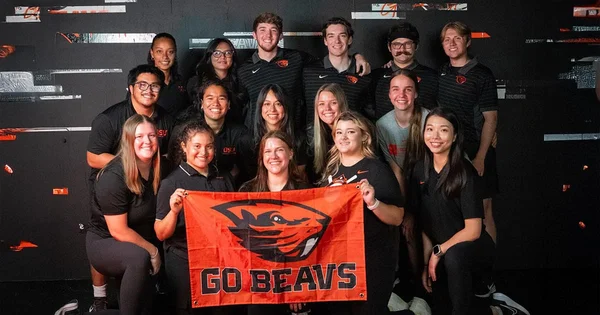 A group of students holding a flag with a beaver logo and the text "GO BEAVS."