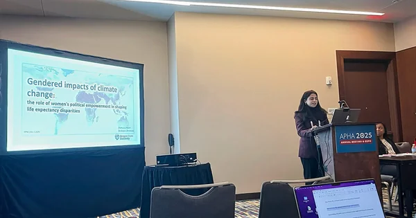 A presenter speaking at a podium during the APHA 2025 conference, with her research title on "Gendered impacts of climate change" displayed on a screen.