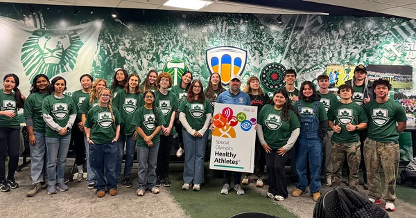 A large group of students in matching green shirts participates in a Special Olympics Healthy Athletes event, symbolizing community service and inclusion in health care.