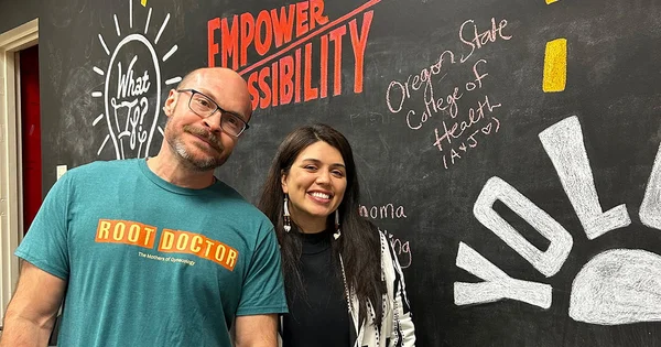 Jonathan and Ashley stand before a chalkboard wall at Partners for Health Equity Summit. The background includes encouraging messages.
