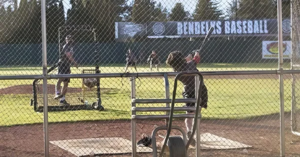Baseball team practice in batting cages, likely for a high school or youth league.