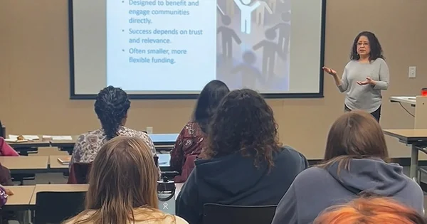 Presenter giving a talk on community engagement, as seen from the audience perspective in a lecture hall.