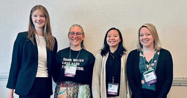 Award recipients pose together at a professional event, wearing name badges and smiling for a group photo indoors.