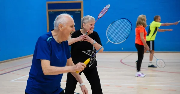Active seniors participating in a recreational indoor badminton match, promoting community fitness and social engagement.