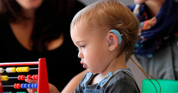 Child with a hearing device focuses intently on learning to count with an abacus, illustrating early educational development and accessibility support.