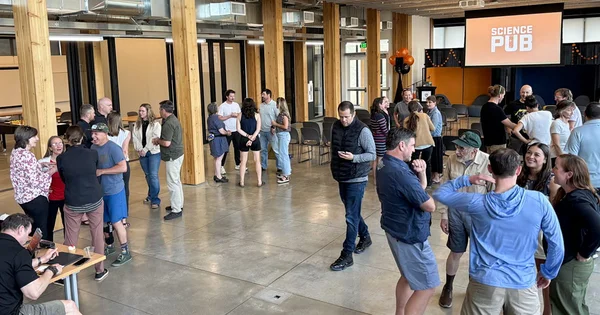 People networking in a modern open space with large wooden pillars and a 'Science Pub' screen in the background.