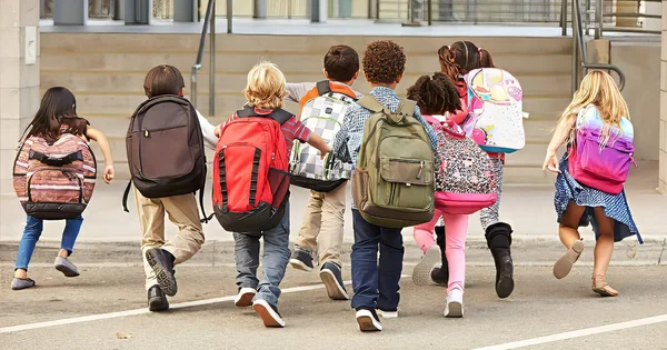 Elementary students enthusiastically running toward a school entrance, signaling the excitement of a school day or return from recess.