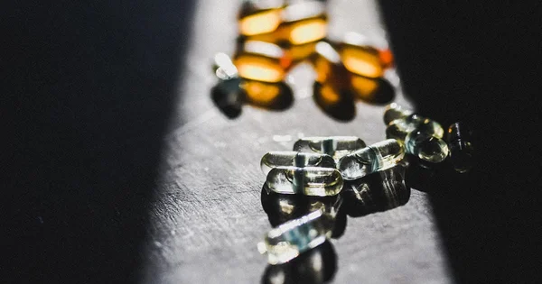 Vitamin E capsules scattered on a dark table, illuminated by a beam of light.