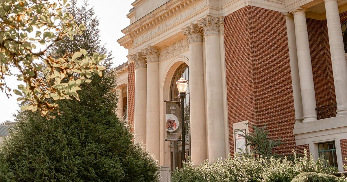 Memorial Union building featuring red brick walls, large white Corinthian columns, and green foliage in the foreground.