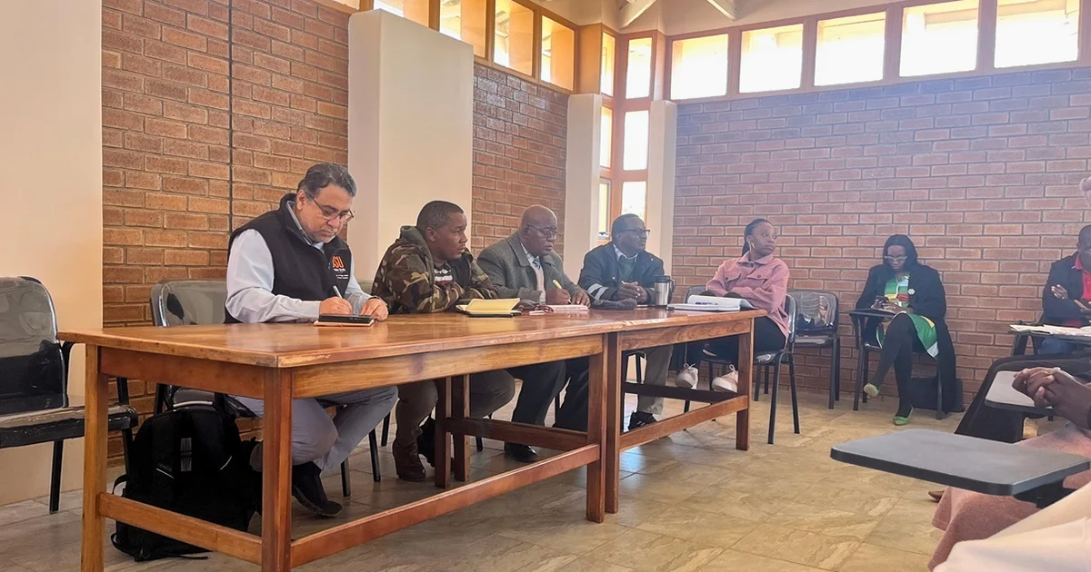 A group of people sitting around a wooden table in a room with brick walls.