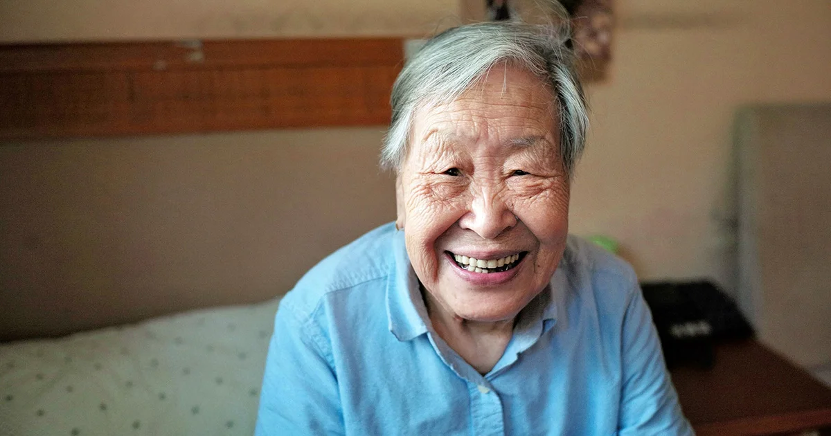 An elderly Asian woman with gray hair smiling warmly at the camera.
