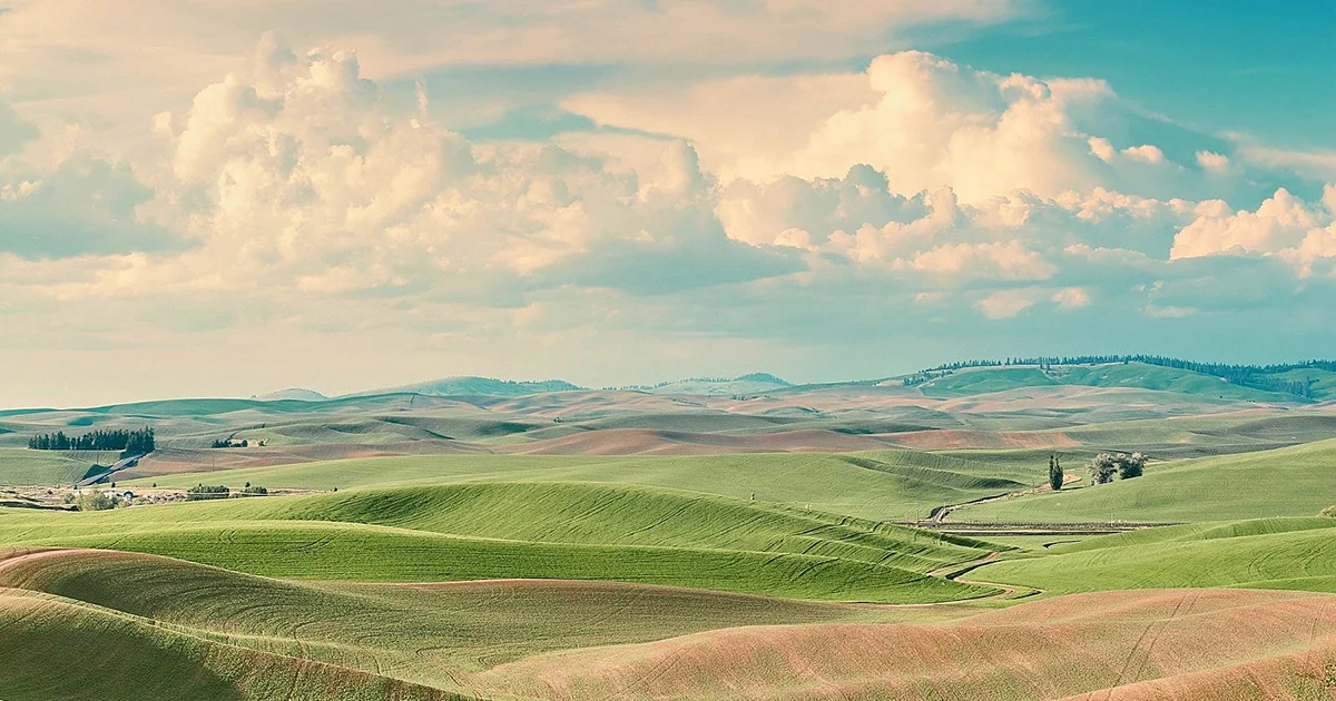 Scenic landscape with rolling hills, green fields, and cloudy sky.