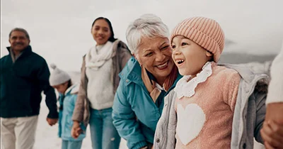 Group of people walking together outdoors, with an older woman and child in the foreground smiling and looking at each other.