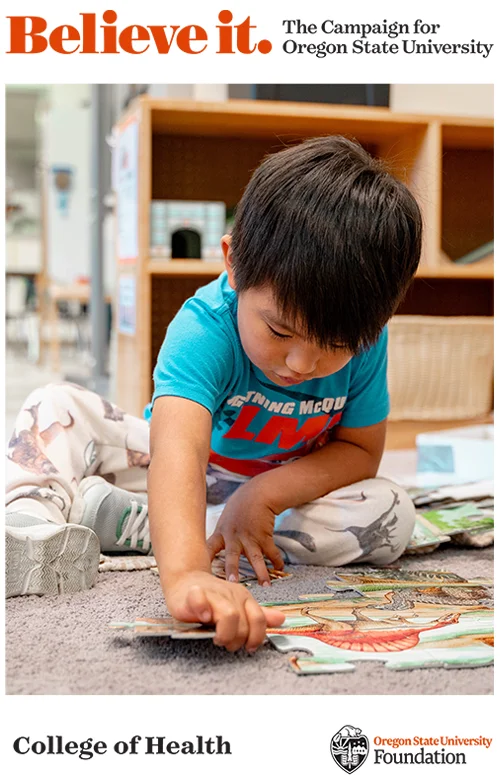Young child in blue shirt sitting on carpet, focused on playing with something on the floor.