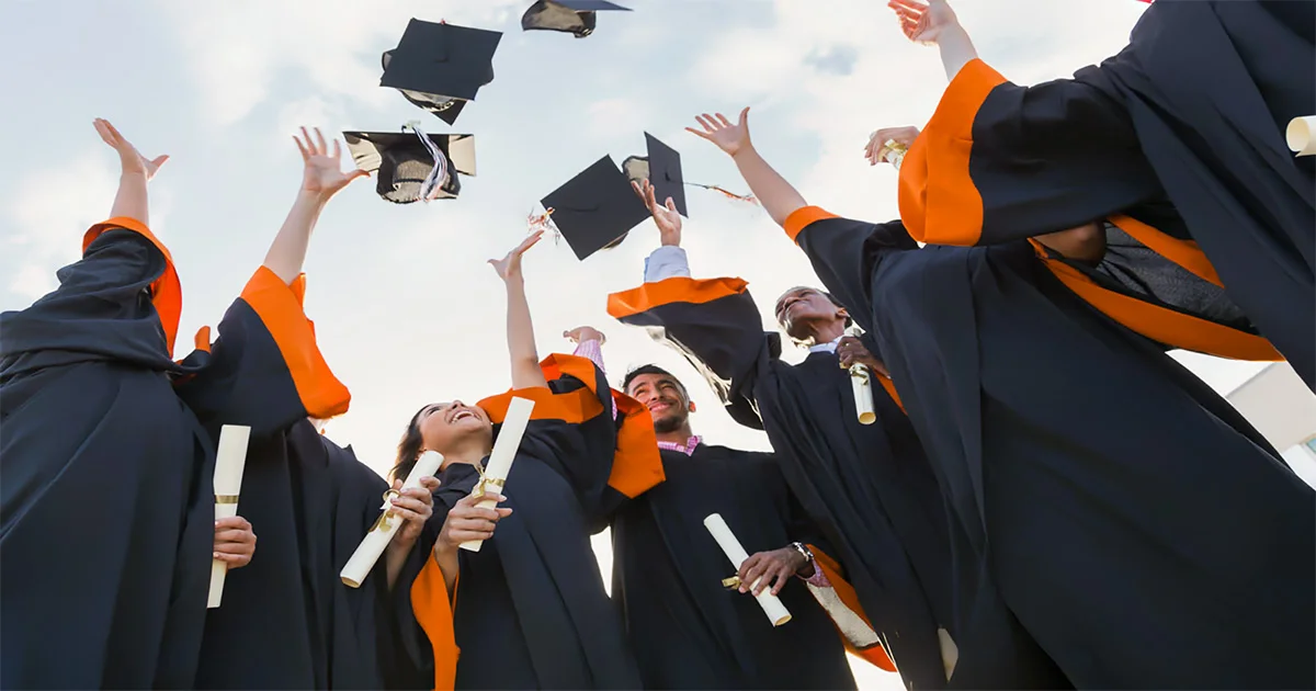 Graduates throwing their graduation caps into the air, viewed from below against a cloudy sky.