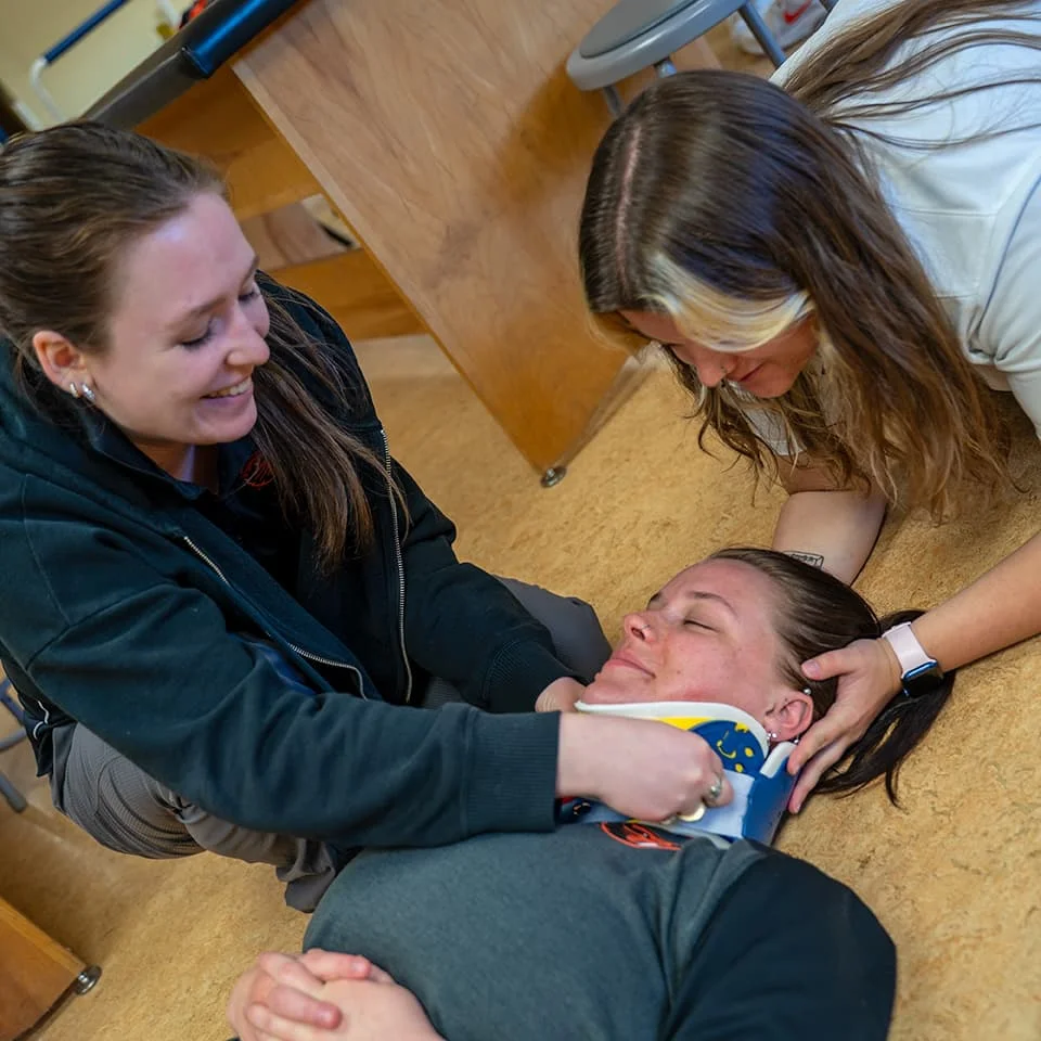 Athletic training students practicing proper application of a neck brace on a simulated patient.