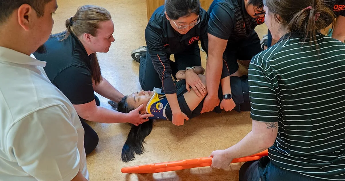 Athletic training students practicing spine boarding techniques on a patient with a cervical collar.