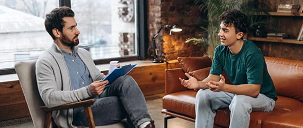 A counselor or therapist listens to a younger client in a session, illustrating a discussion or consultation in a professional yet relaxed environment.