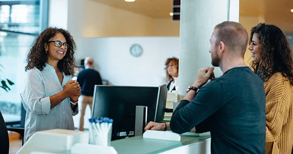 A professional working in health promotion or a service role assists or advises two clients at a desk, illustrating health interaction or patient service.