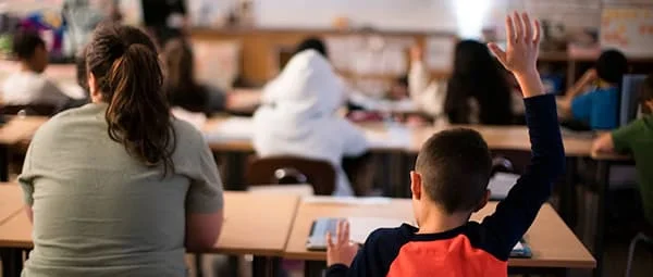 A young student in a classroom raises their hand to answer a question.