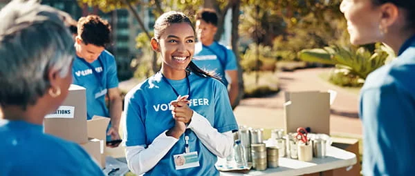 A smiling young volunteer talks with a community member at an outdoor charity event.